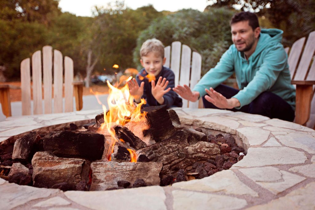 father and son warming their hands around a stone fire pit