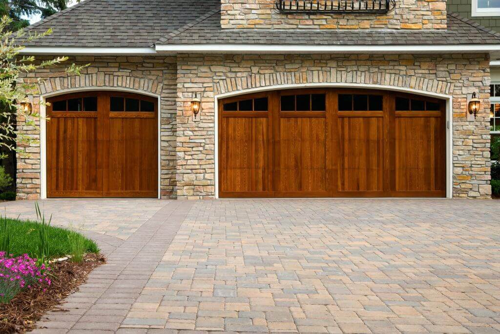 stone garage with wooden doors and paver driveway